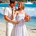 A romantic wedding scene featuring a bride and groom on a beach in Seychelles, with a boat visible in the background.