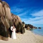 Newlyweds on a beach in Seychelles, surrounded by large rocks, capturing the essence of their romantic honeymoon.